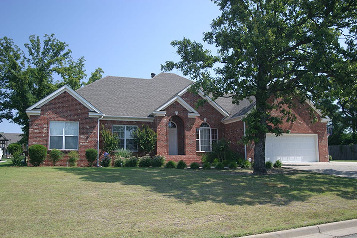 House plan exterior: One-story brick home with gabled roof, arched entry, and attached two-car garage.