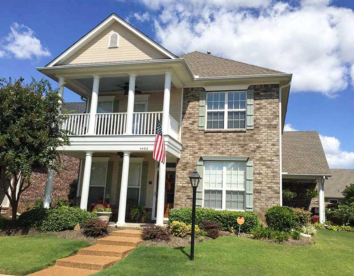 Two-story house plan exterior with brick and vinyl siding, covered front porch with columns, and multi-pane windows.