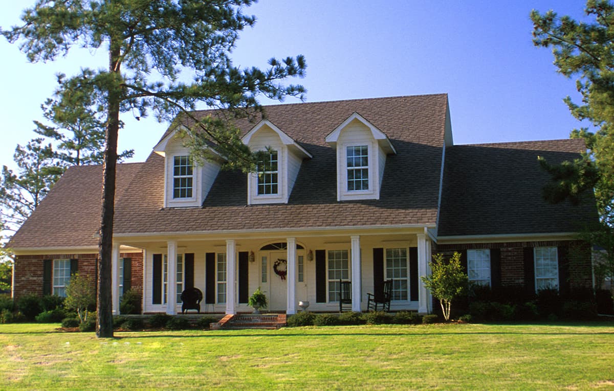 House plan exterior with a hip roof, full-width covered porch supported by columns, and three prominent dormers.
