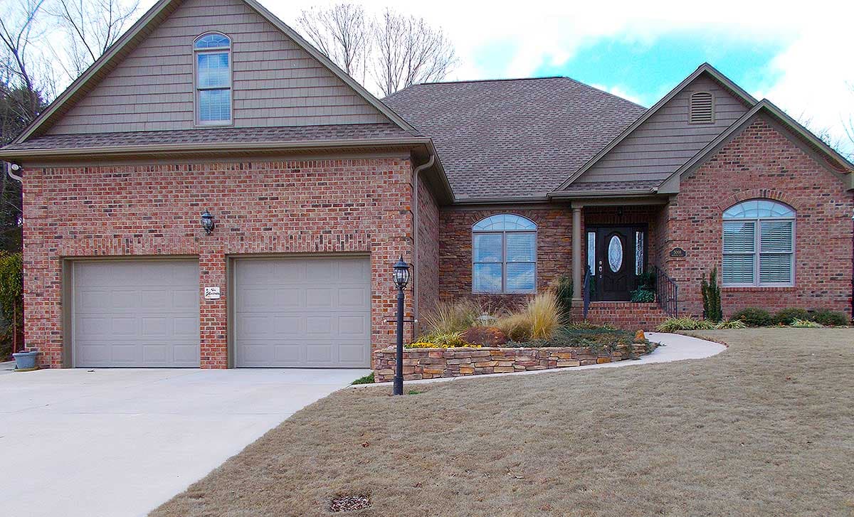 House plan exterior: Brick home with two-car garage, arched windows, dormer, and covered entry.
