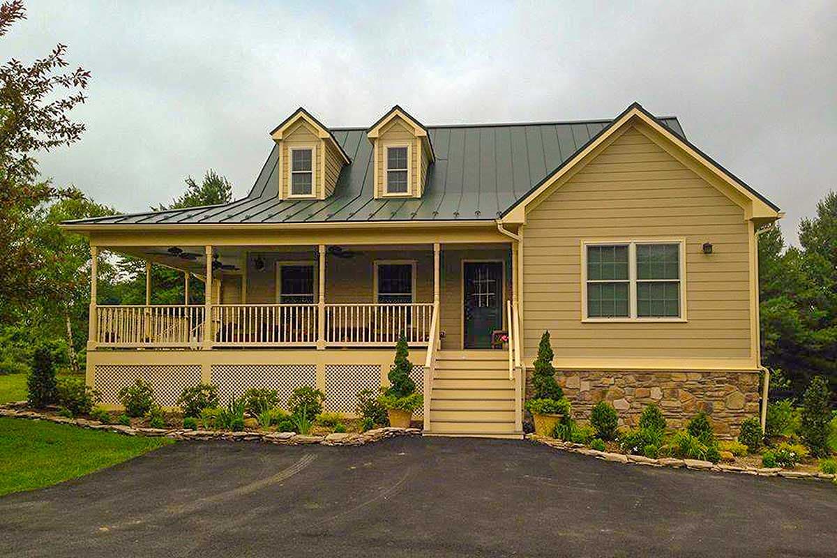 House plan exterior with wraparound porch, metal roof, dormers, and stone foundation.