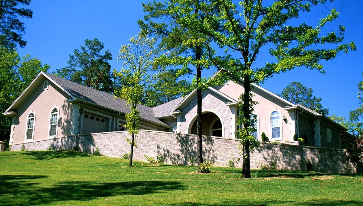 House plan exterior: one-story residence with arched entry, stucco facade, brick accents, dual-pane windows, and attached garage.