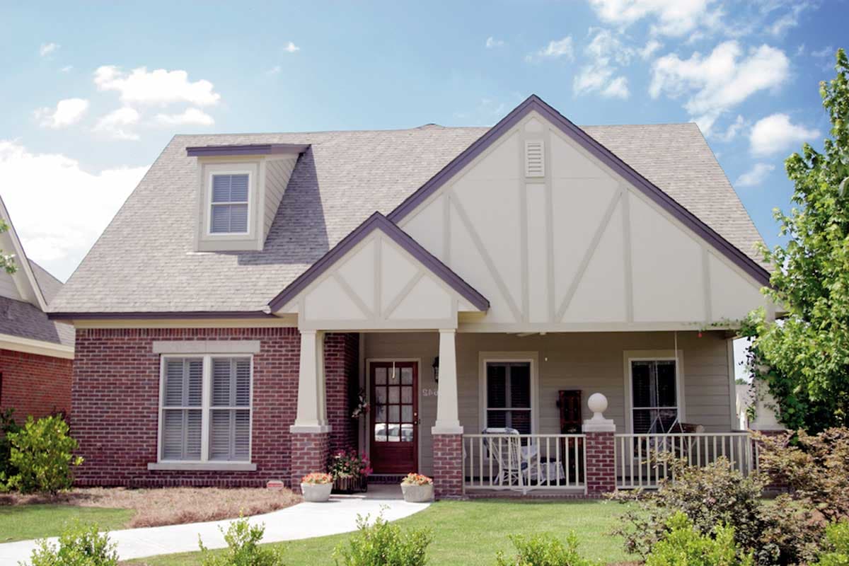 House plan exterior: one-and-a-half stories, brick facade, gable dormer, and covered front porch with brick pillars.