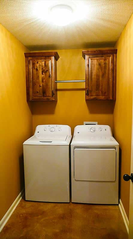 Laundry room with white washer and dryer, wood cabinets above, and hanging rod.