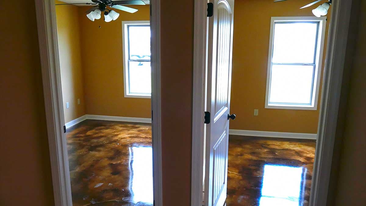 View of two rooms with stained concrete floors, ceiling fans, and windows. A white door is open.