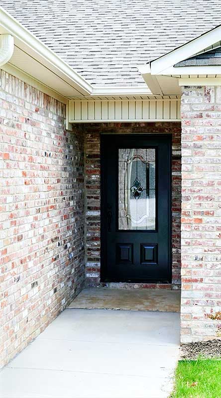 House plan exterior: Red brick facade with a black front door featuring decorative glass and two lower panels.