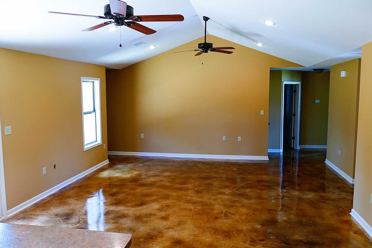 Interior view of a house with vaulted ceilings, two ceiling fans, a single window, and stained concrete flooring.