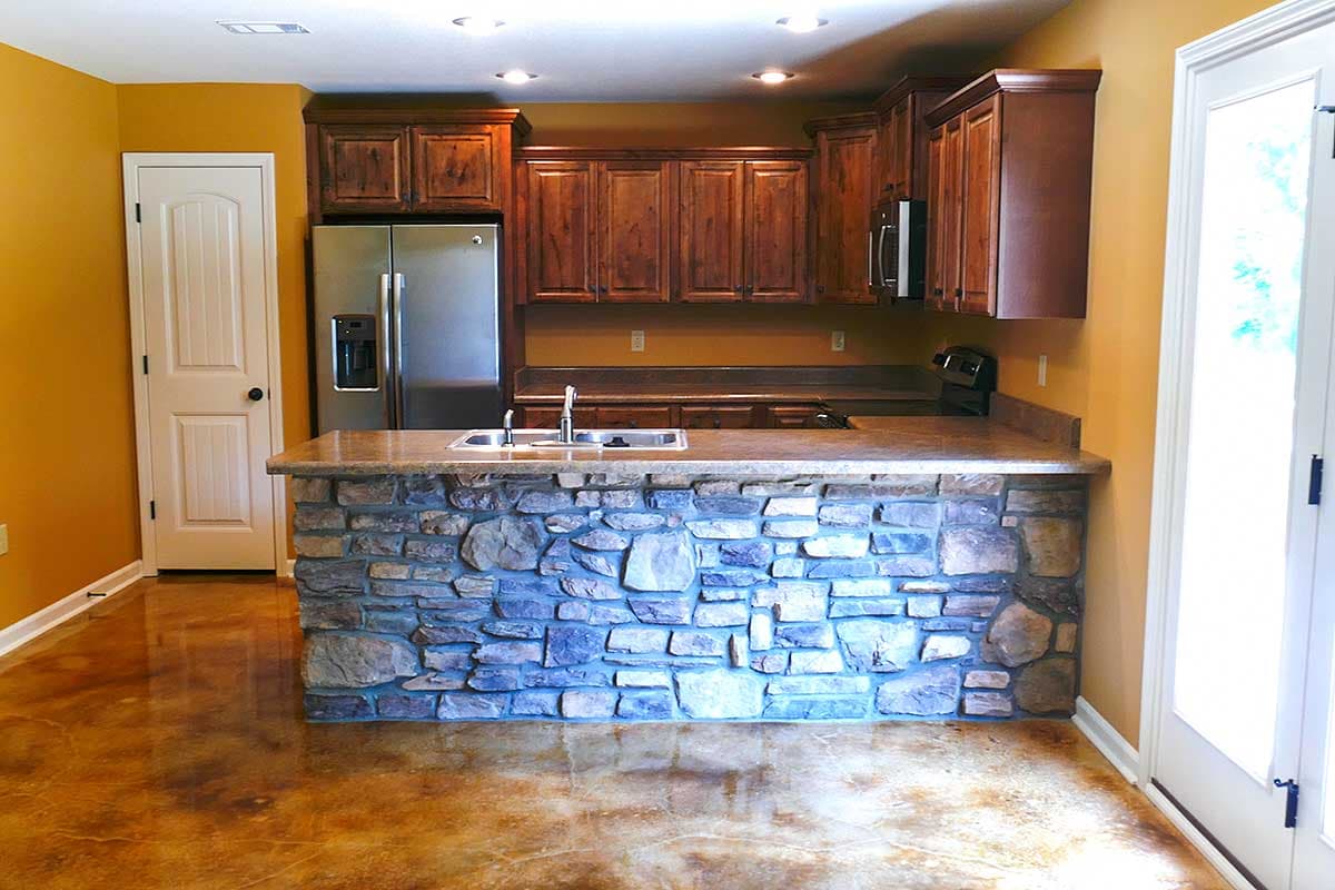Kitchen with wood cabinets, stainless steel refrigerator, granite countertops, and stone-faced island.