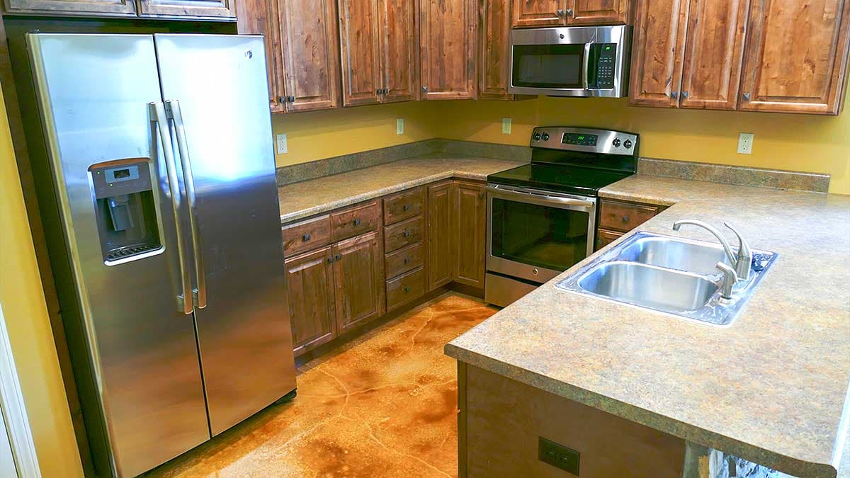Kitchen featuring stainless steel refrigerator, double sink, range, microwave, and wood cabinetry with a concrete-look countertop.