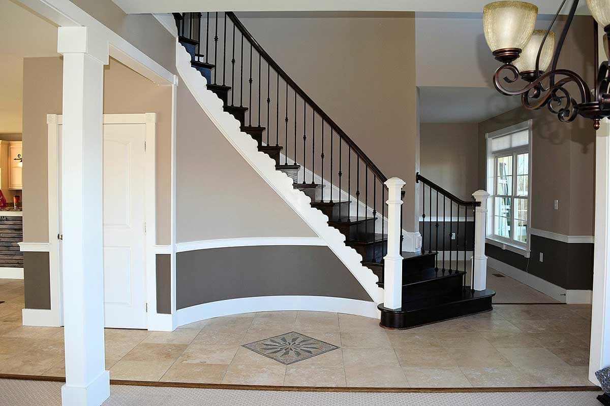 Interior view of a grand foyer with a curved staircase featuring dark wood treads and black balusters, large tiled floor, and white columns.