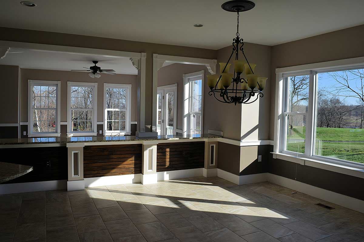 Interior view of a house plan, showing a kitchen or dining area with a breakfast bar, large windows, and a chandelier.