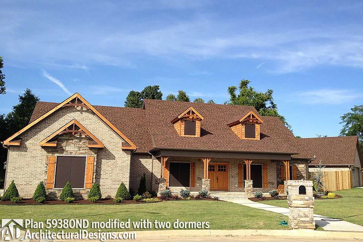 House plan exterior with brick facade, prominent gables, exposed wooden beams, covered porch, and two dormers.