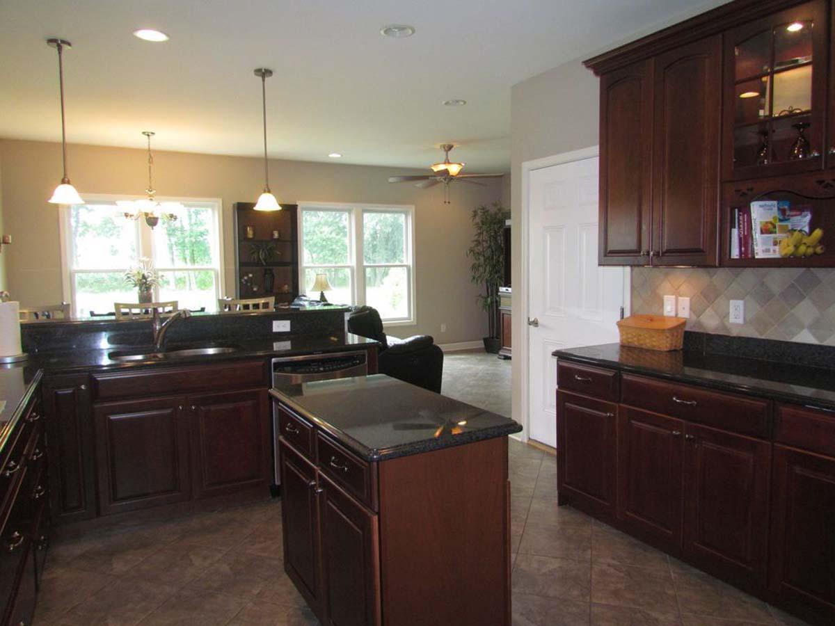 Kitchen with dark wood cabinets, granite countertops, island, stainless steel dishwasher, and open access to a dining area and living space.