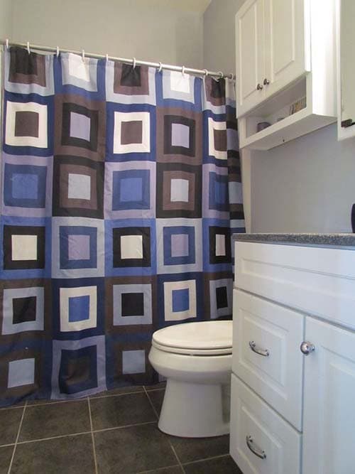 Bathroom interior with geometric shower curtain, white vanity, toilet, and dark tile floor.