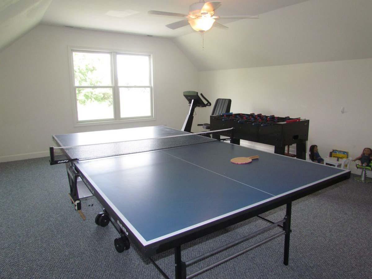 Finished attic room with ping pong table, foosball table, treadmill, and pitched ceiling.