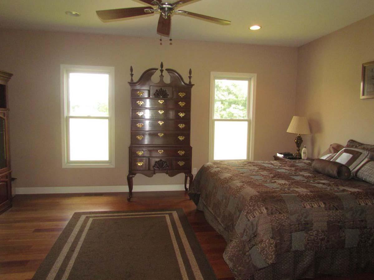 Bedroom with bed, tall chest, ceiling fan, recessed lighting, and two double-hung windows.