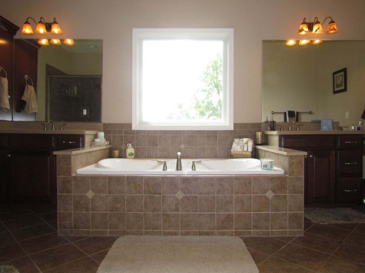 Bathroom with built-in tub, double vanity with dark wood cabinets, and large window.