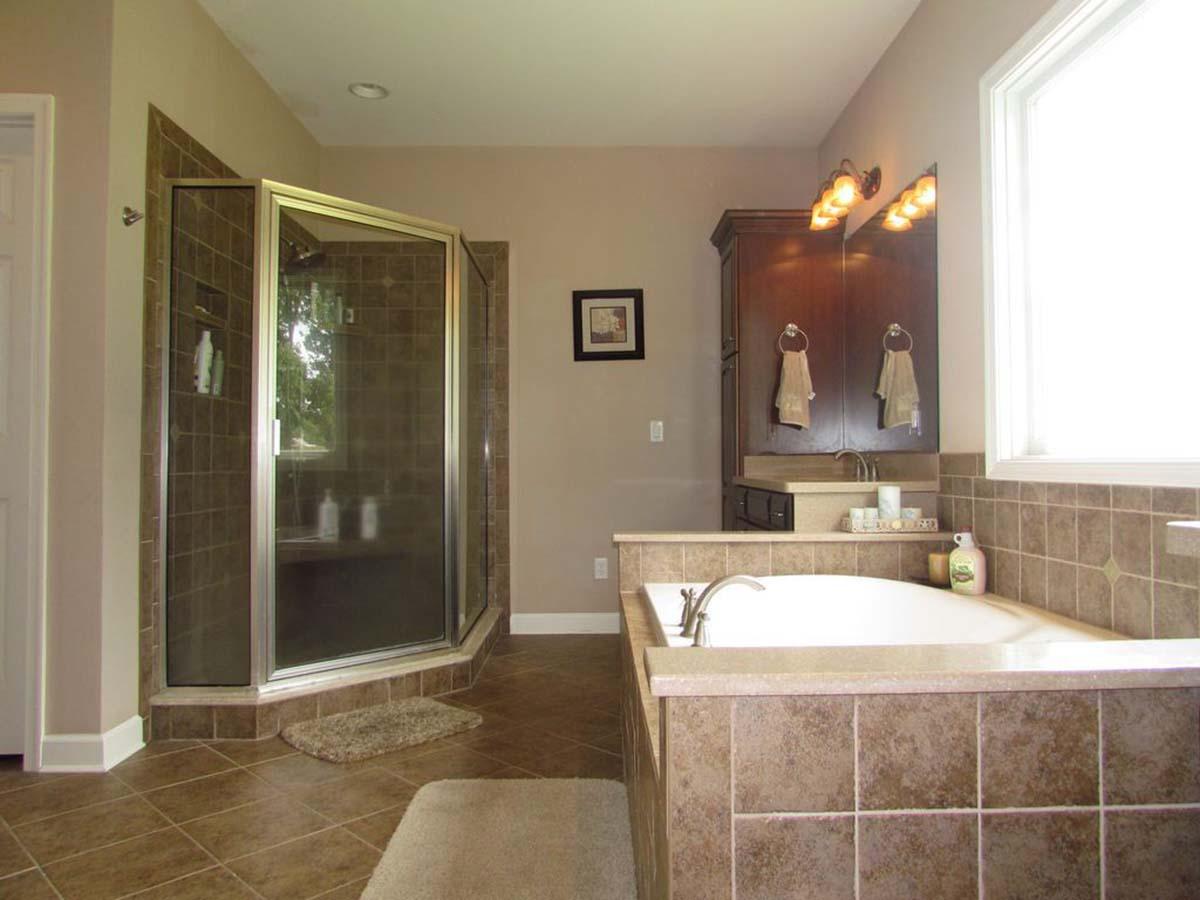 Bathroom with corner glass shower enclosure, tiled tub surround, vanity with dark wood cabinets, and a large window.