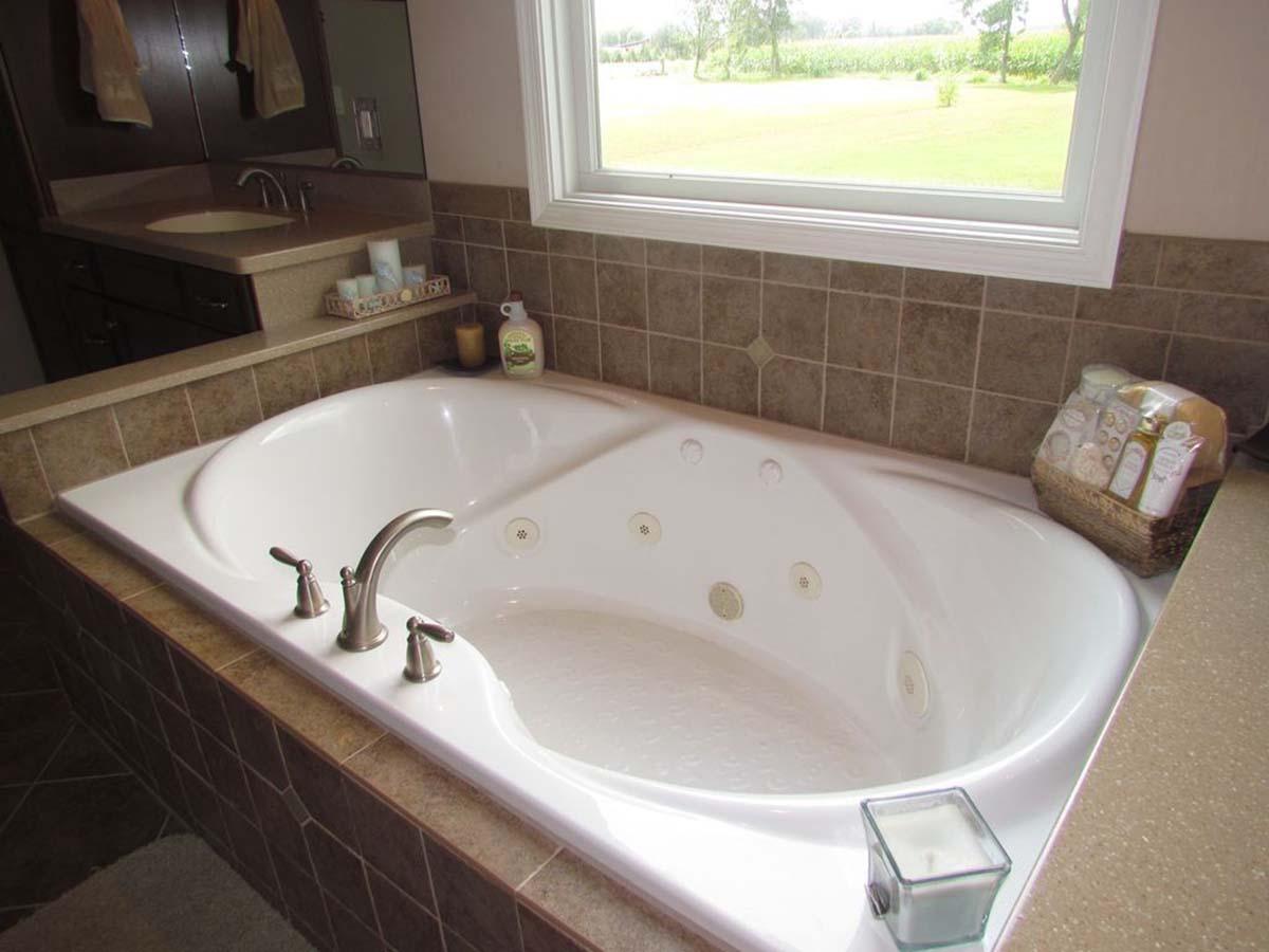 Interior view of a bathroom featuring a built-in soaking tub with a single faucet and jets, tiled surround, and a large window overlooking a field.
