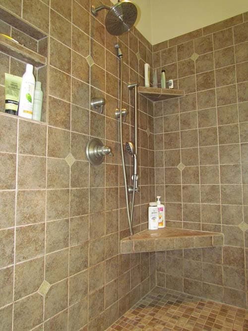 Tiled shower with corner bench, multi-head shower fixture, and recessed niche shelves.