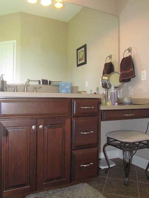 Bathroom vanity with dark wood cabinets, double sink, granite countertop, and a makeup vanity with stool.