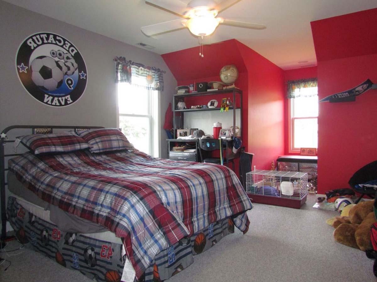 Bedroom with bed, desk, shelves, and sloped ceiling. Features soccer-themed decor and red accent walls.