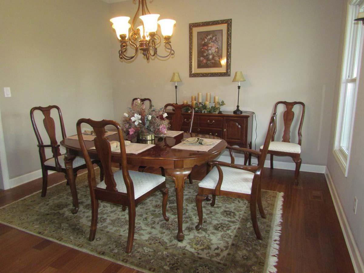 Dining room with oval table, six chairs, buffet, chandelier, and botanical wall art.