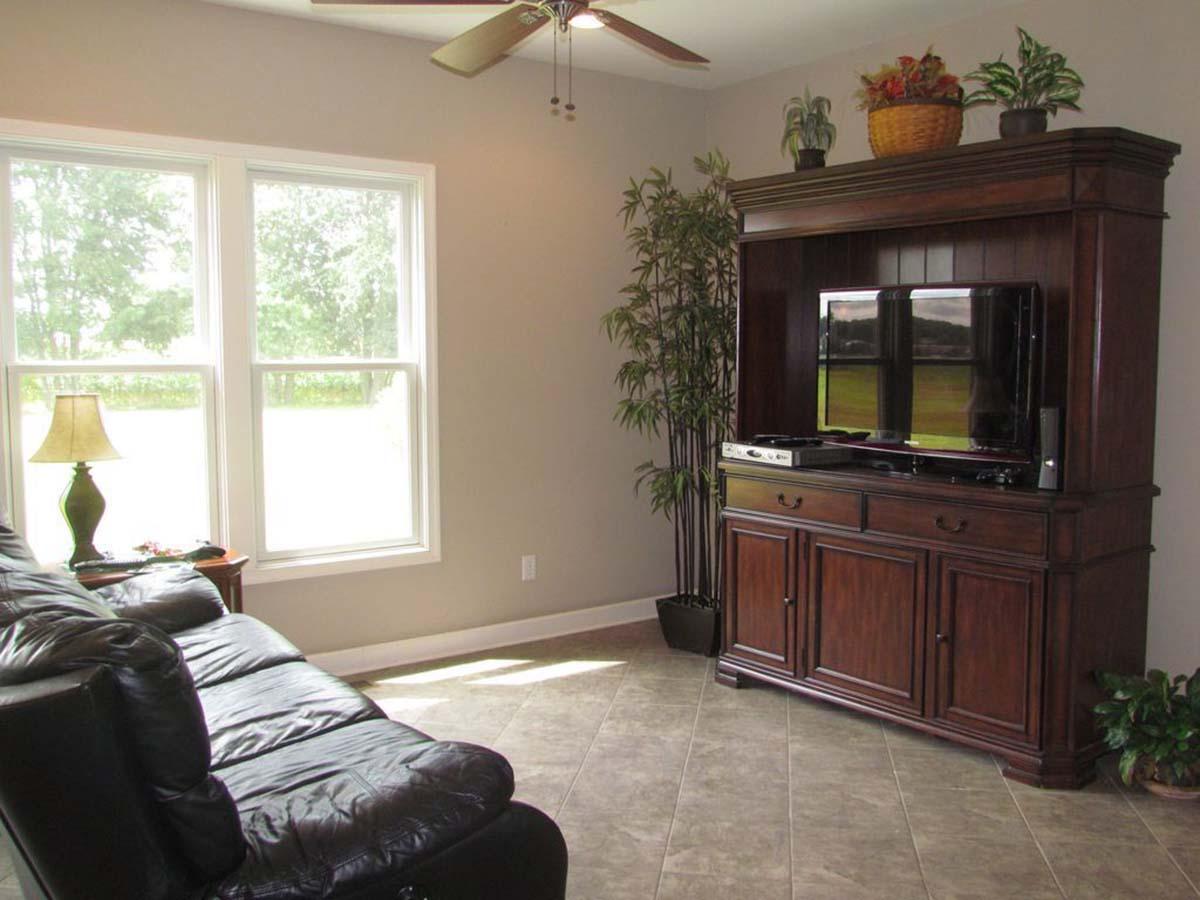 Living room interior with black leather sofa, large windows, and wooden entertainment center with television.