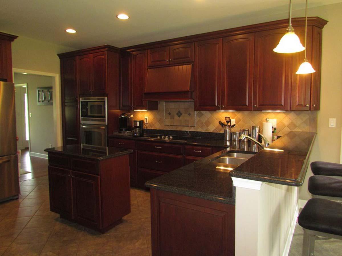 Kitchen with dark cherry cabinets, granite countertops, island with storage, stainless steel appliances, and pendant lighting.