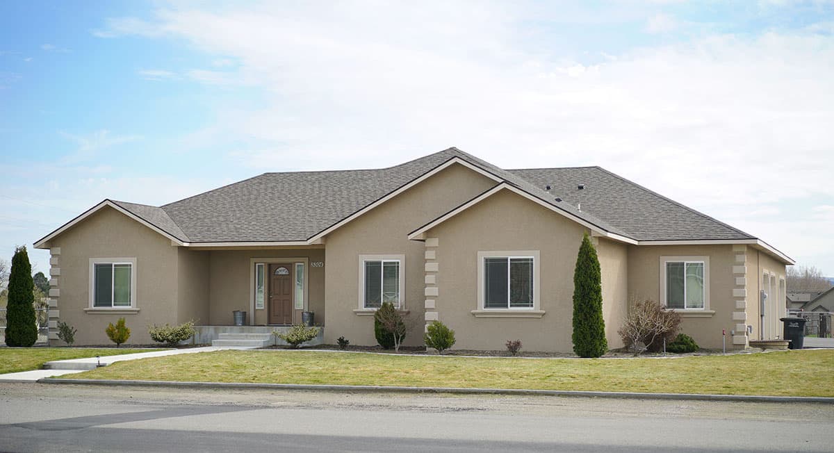 One-story house plan exterior with a prominent gable roofline, central entry, multiple windows, and decorative corner accents.