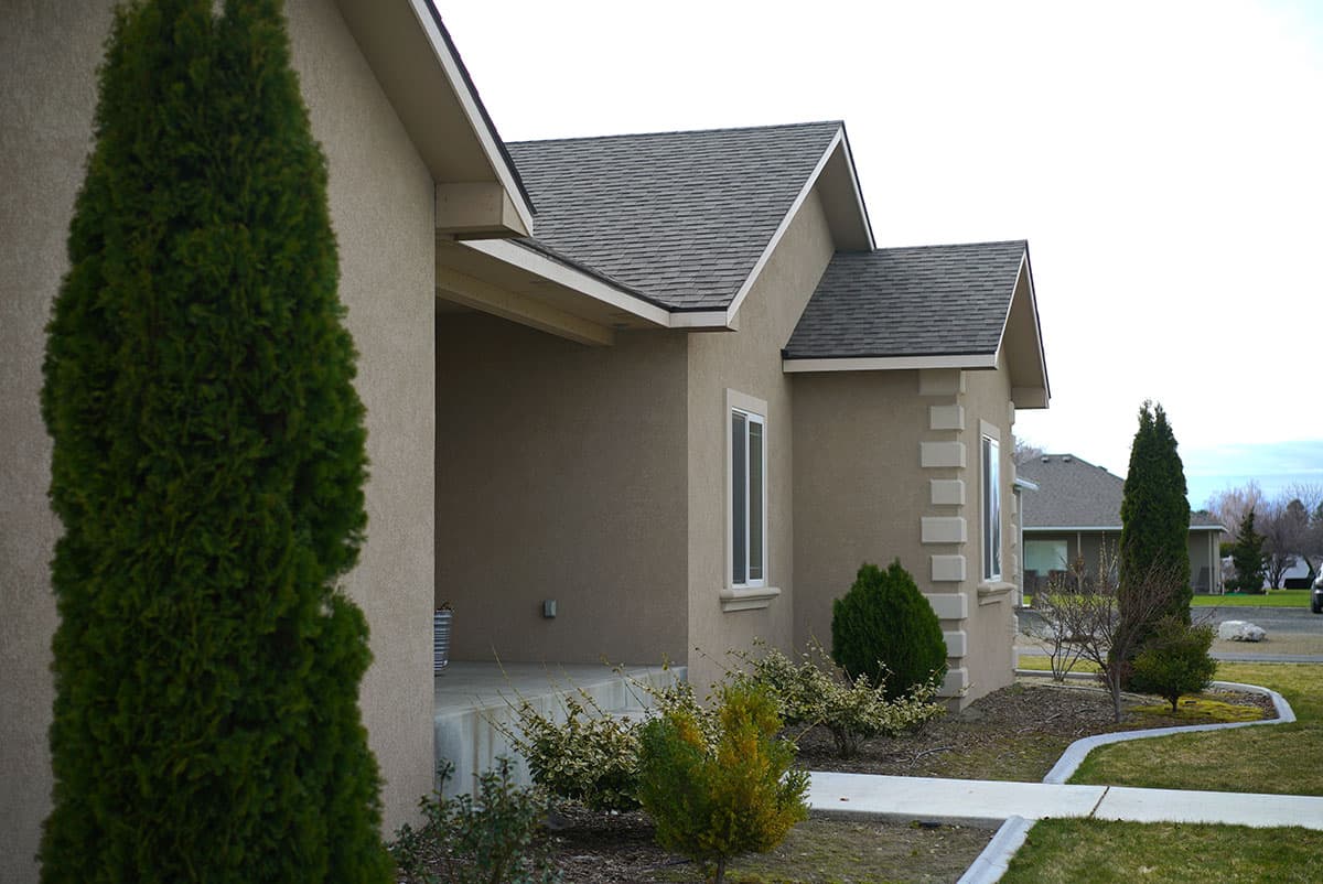 House plan exterior, stucco finish, gabled rooflines, and decorative stone accents around windows.