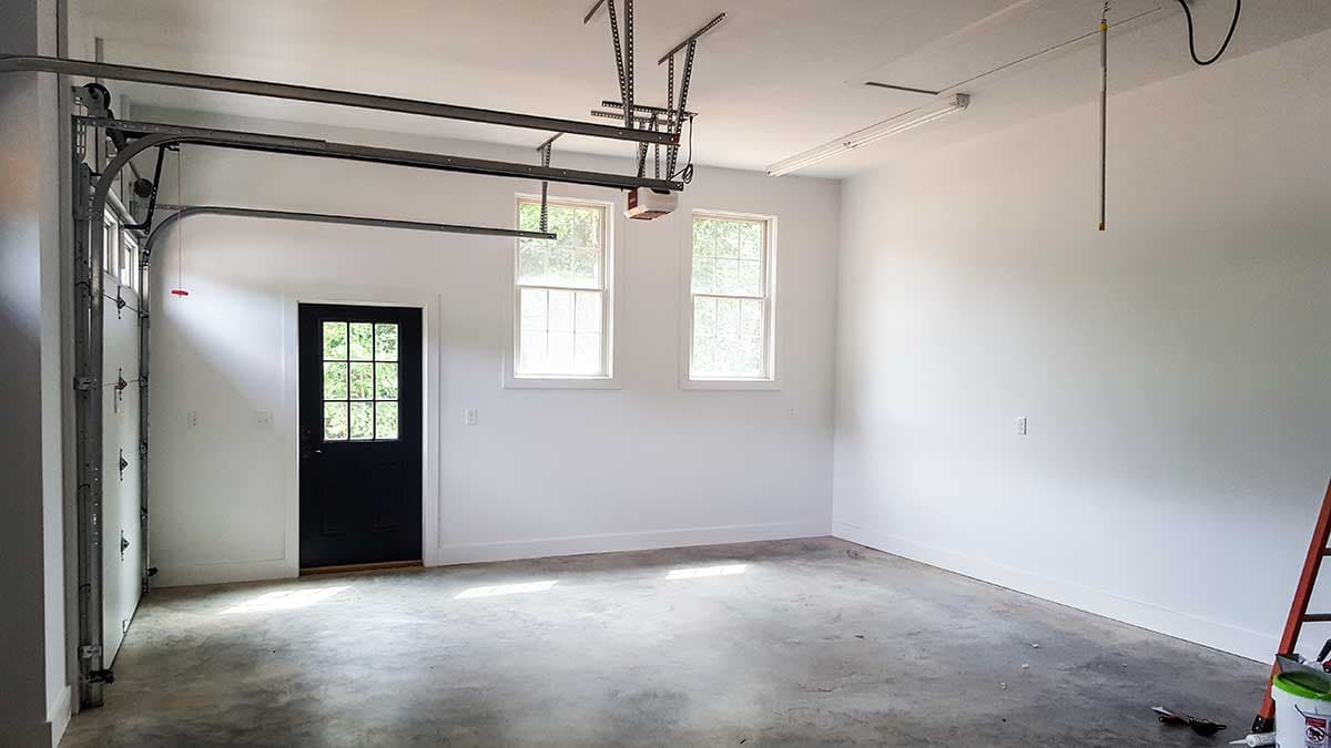 Garage interior with a paneled garage door, black entry door with windows, and two double-hung windows.