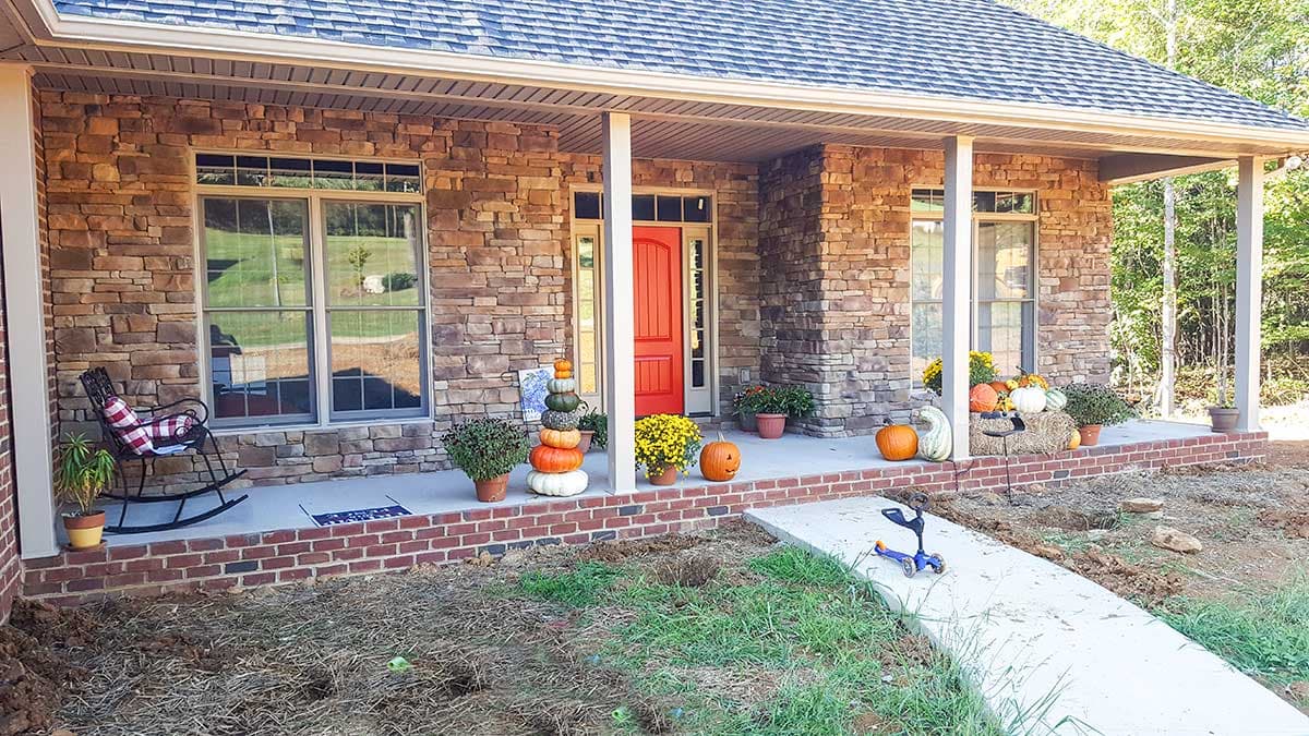 House plan exterior: Ranch style with stone facade, covered front porch with white columns, red double-door entry, and multiple windows.