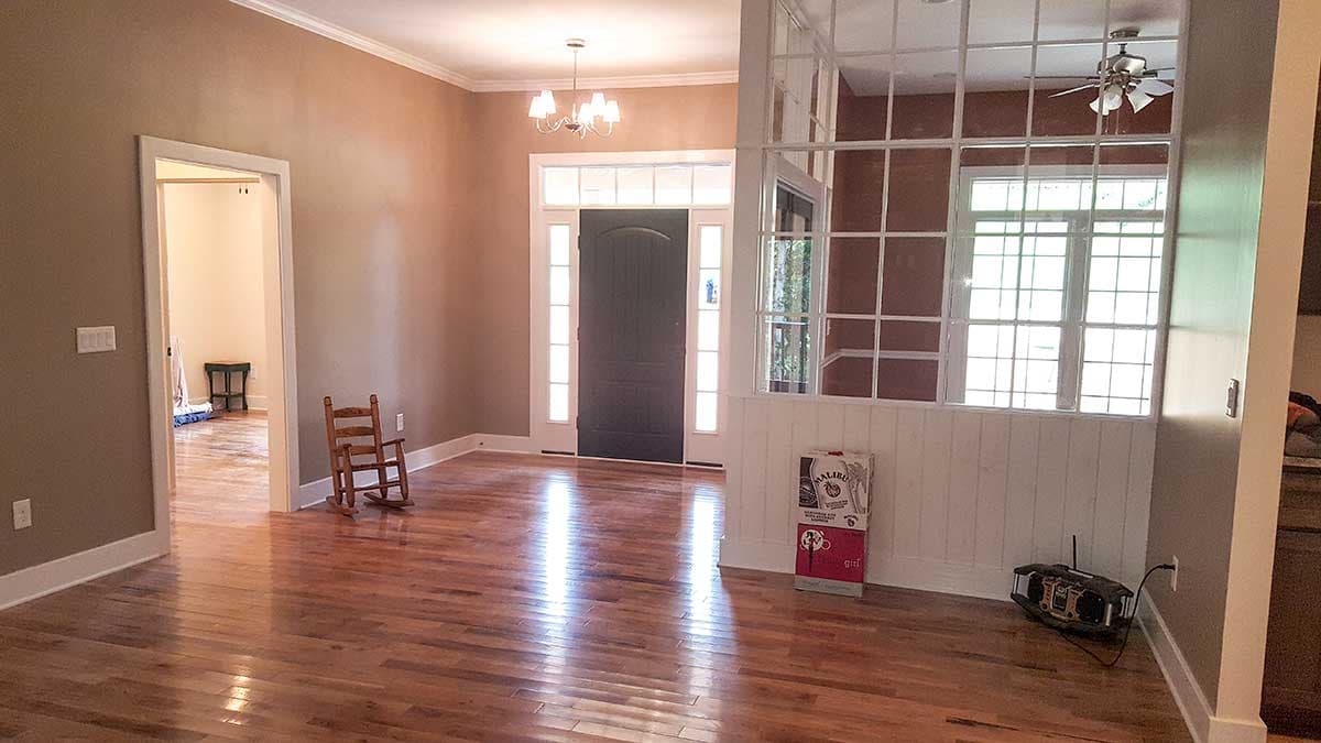 Interior view of a house foyer with a dark front door, sidelight windows, chandelier, and a room divider with multi-pane windows.