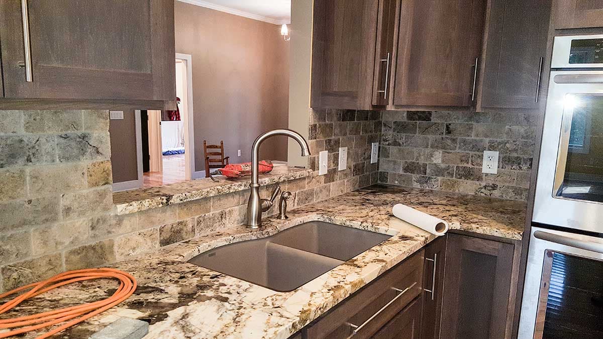 Kitchen with granite countertops, double basin sink, stone tile backsplash, and dark wood cabinetry.