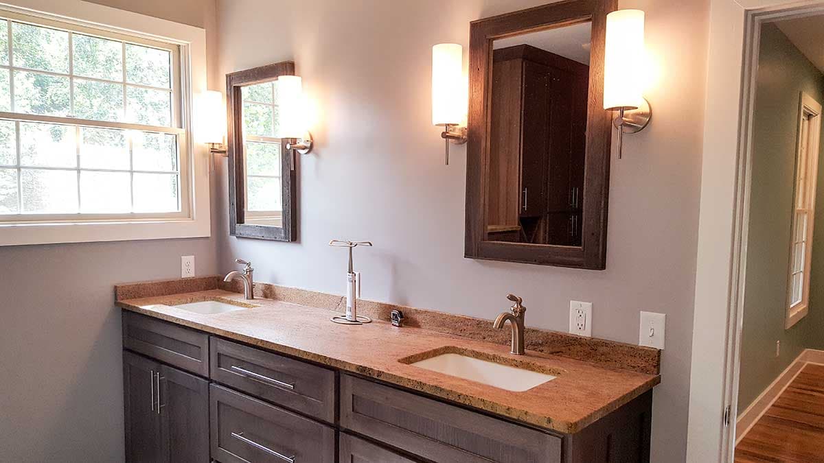 Double vanity with granite countertop, dual sinks, and wood-framed mirrors with wall sconces.