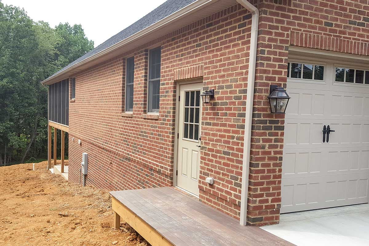 House plan exterior with red brick siding, screened porch, attached garage, and a wooden deck.