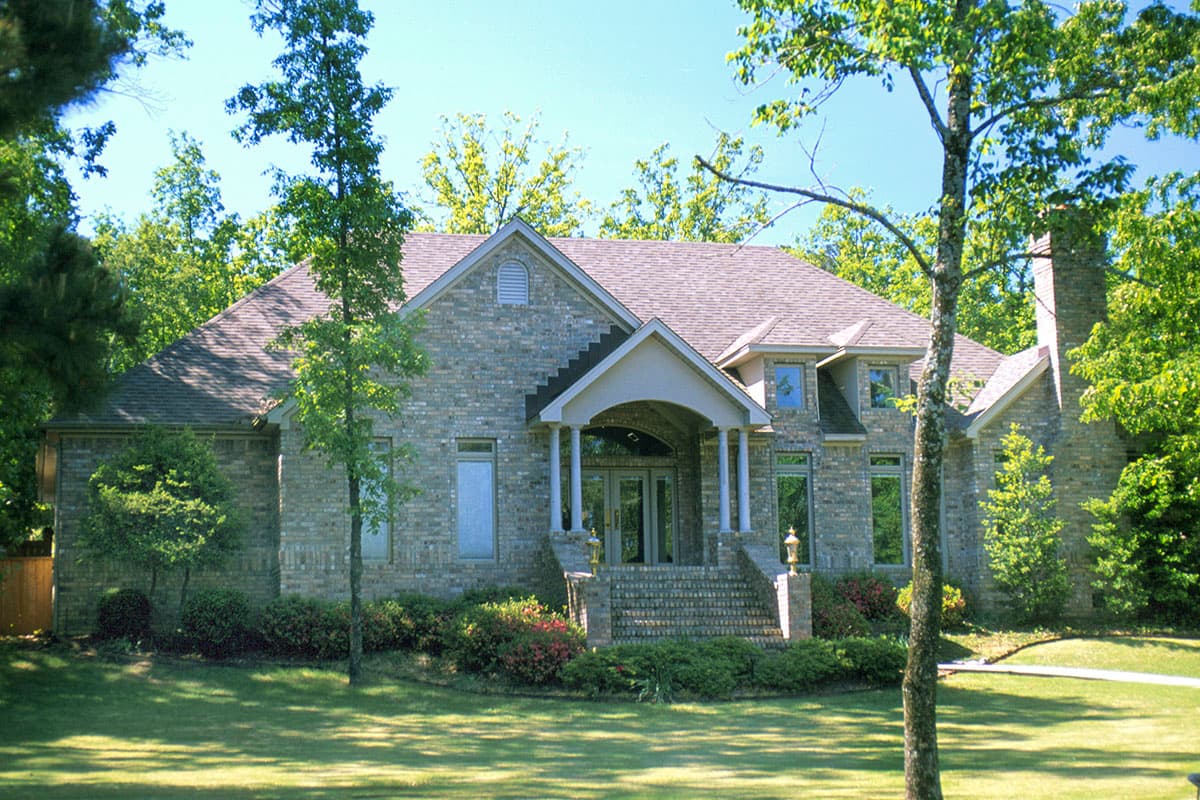 House plan exterior with brick facade, prominent gables, covered entry with columns, and a substantial stone chimney.