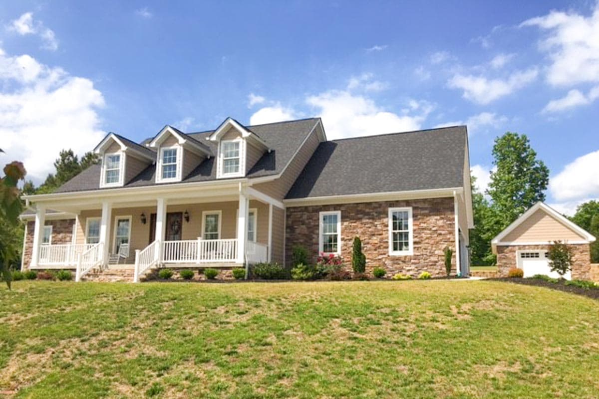 House plan exterior with a wrap-around porch, dormer windows, stone accents, and a detached garage.