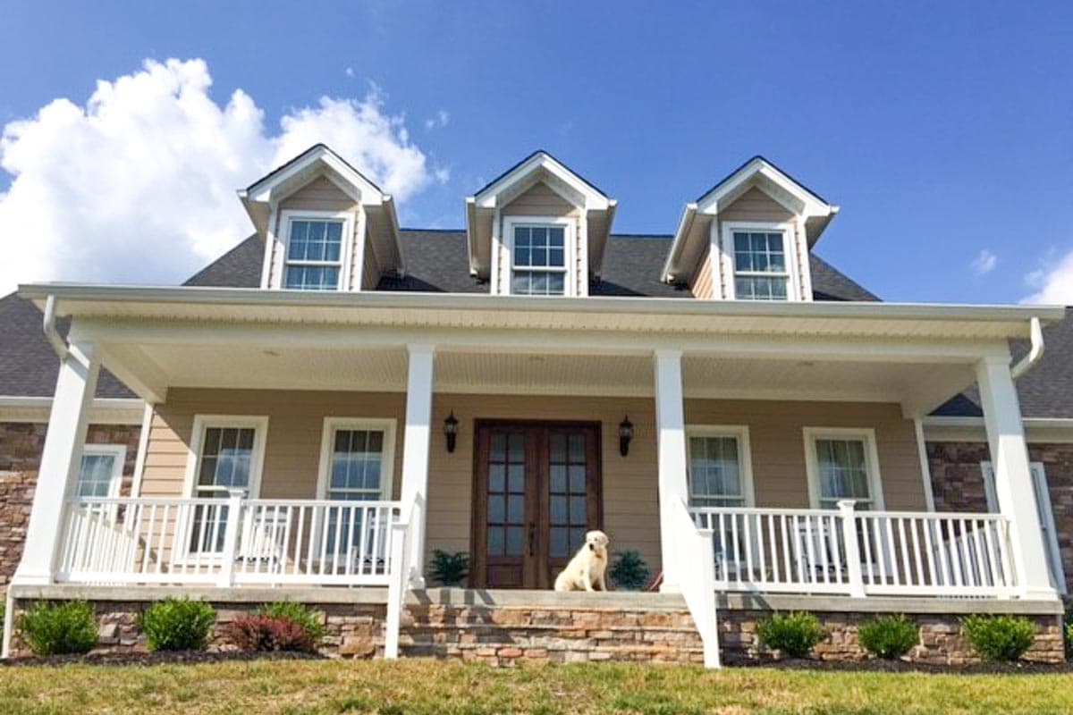 House plan exterior: Two-story home with full-width covered porch, multiple gables with dormer windows, and stone accents.