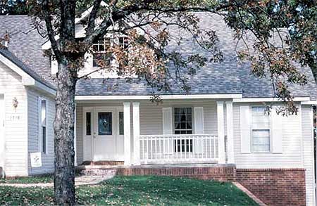 House plan exterior: Two-story home with a covered front porch supported by four square columns and a white railing.