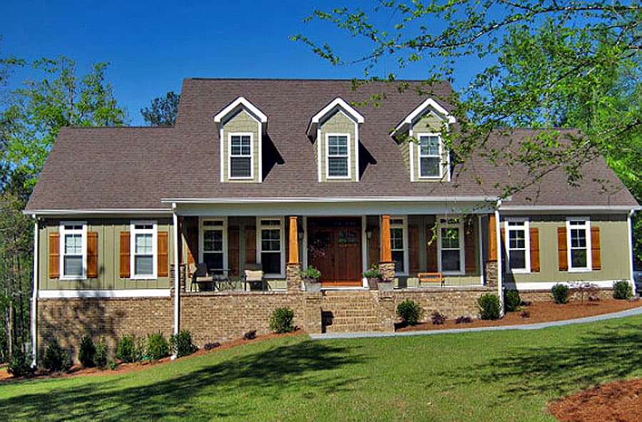 House plan exterior with a wide covered porch, brick base, dormers, and wooden shutters.