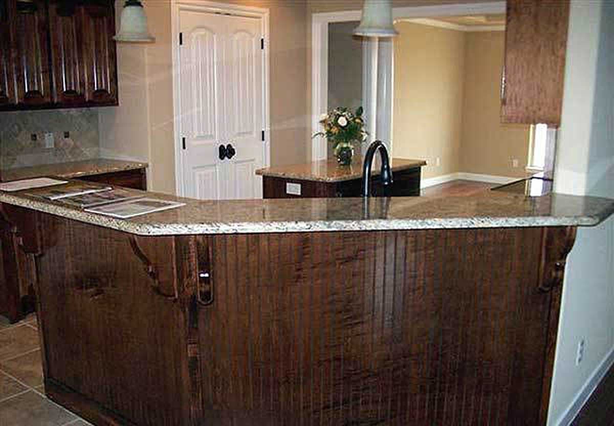 Kitchen island with sink and granite countertop, dark wood paneled base, and decorative brackets.