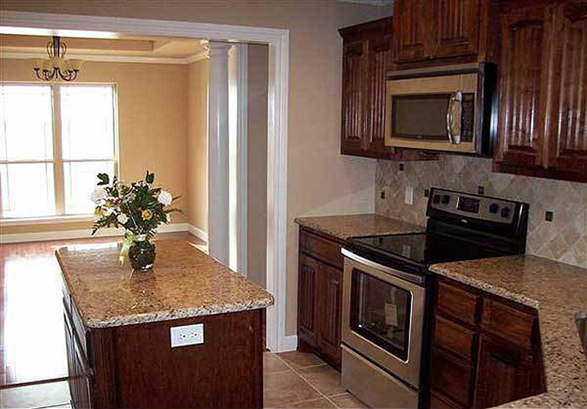Kitchen with granite countertops, wooden cabinets, stainless steel range, and an island with a vase of flowers.