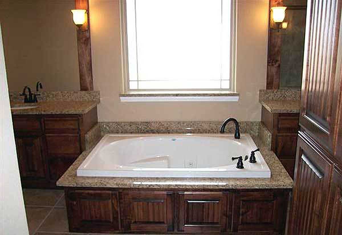 Bathroom with drop-in tub, granite surround, wooden vanity cabinets, and a large window above the tub.