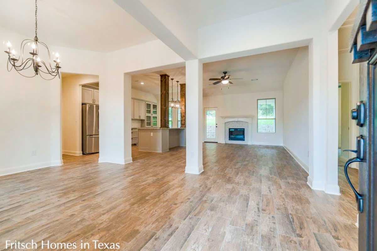 Interior view of living room with fireplace and kitchen, showing columns, wood-look tile flooring, and ceiling fan.