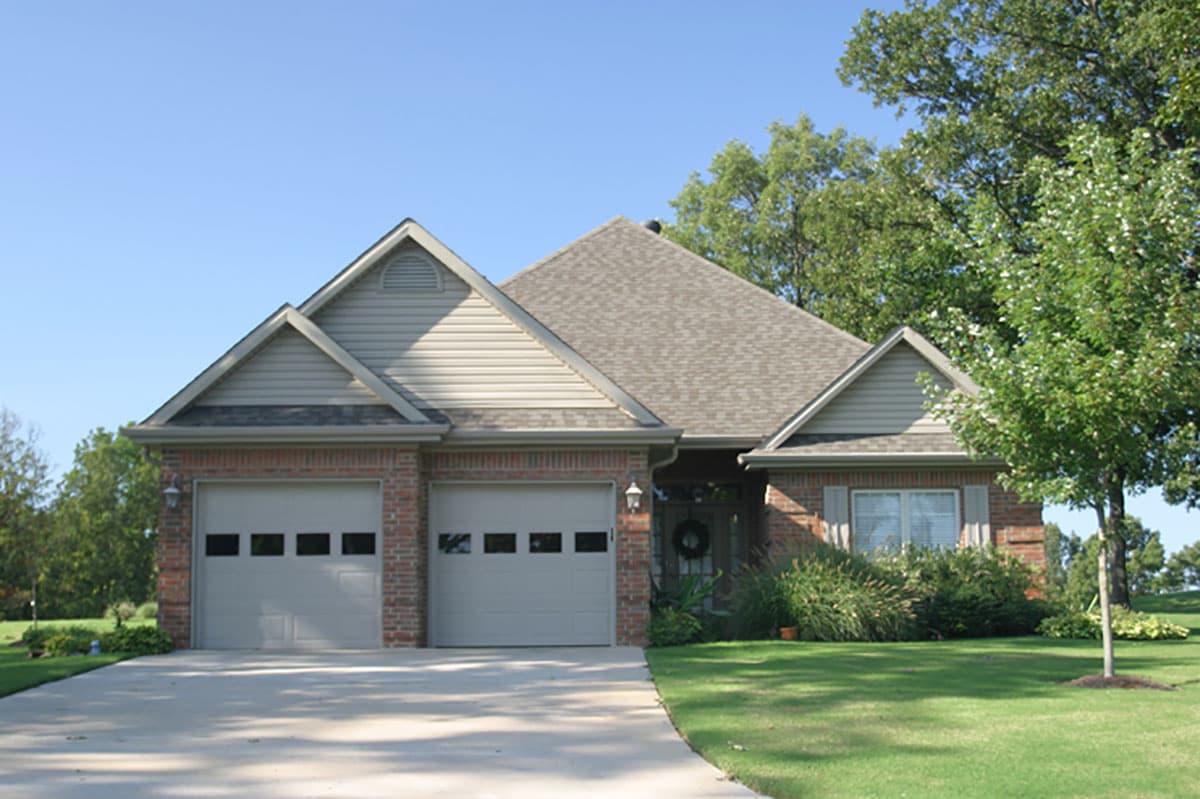 House plan exterior featuring a brick facade, two-car garage, prominent gables, and a hip roof.
