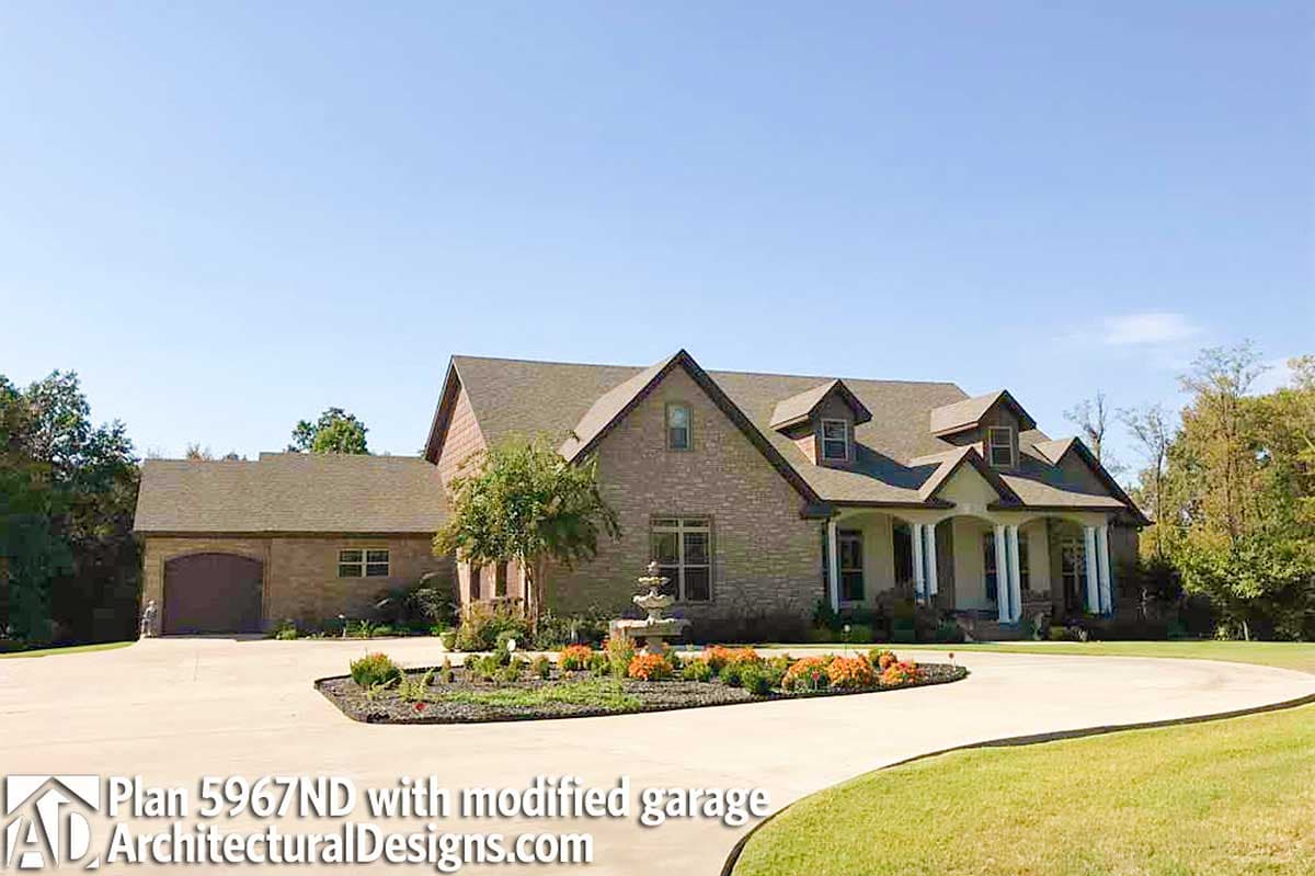 House plan exterior: Two-story brick home with gabled dormers, covered porch with columns, and attached garage.