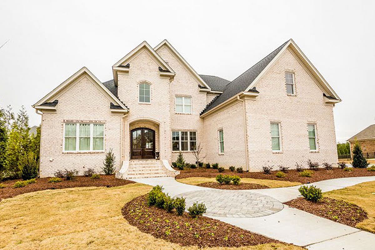 House plan exterior: Two-story brick home with arched entryway, multiple gables, and a curved paver driveway.