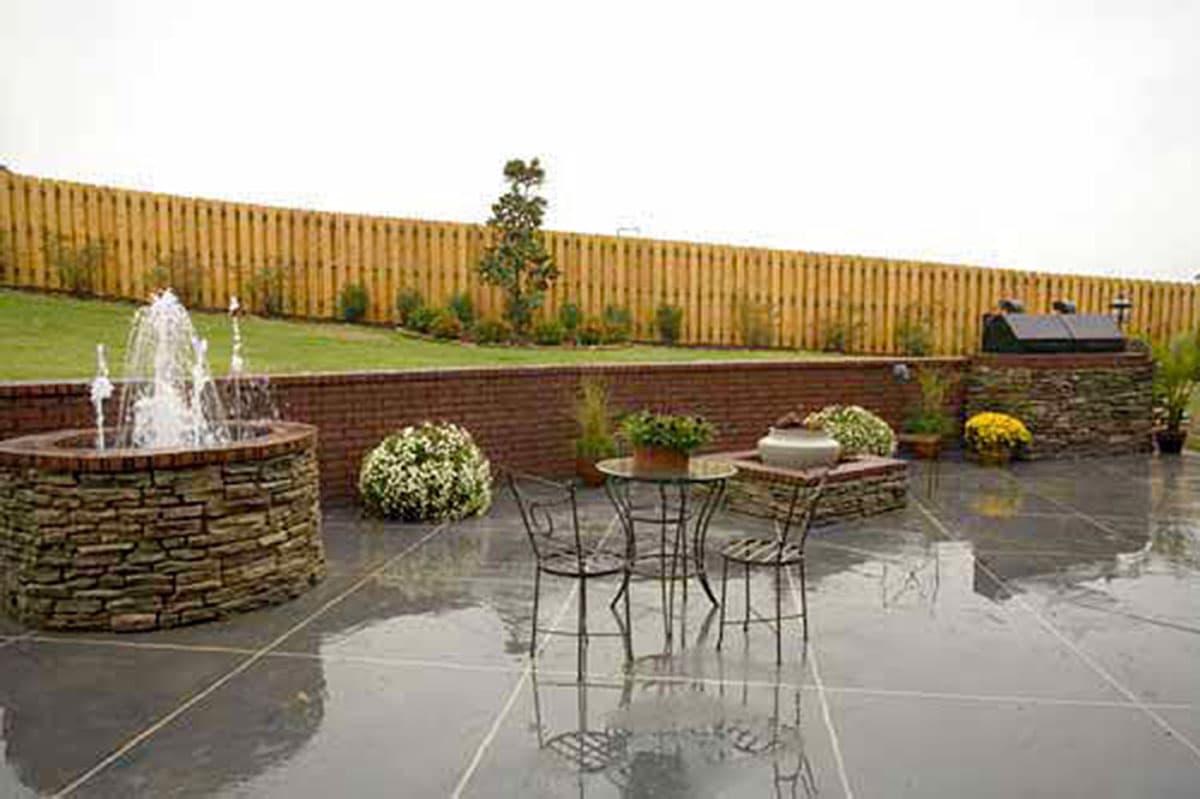 Patio with stone fountain, seating area, outdoor grill, and wooden privacy fence.